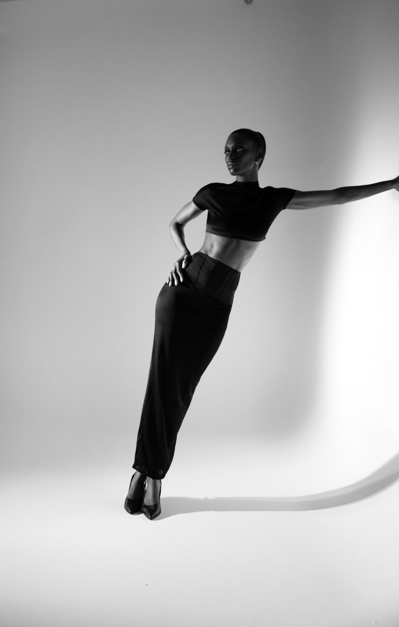 Mannequin de profil en mouvement, bras tendus, portant le top noir 03.87 dans un studio clair