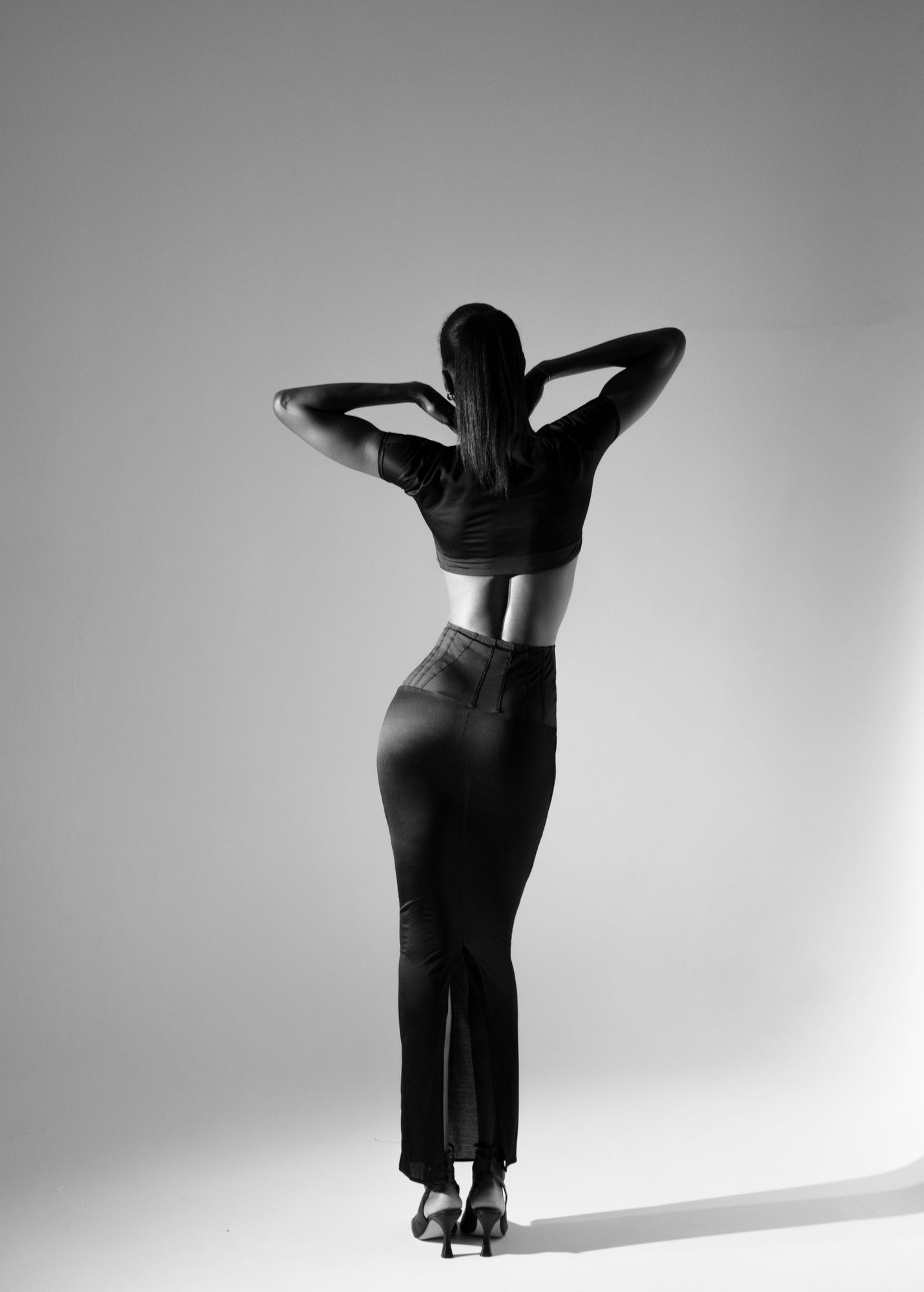 Mannequin vu de dos portant la jupe longue noire 03.87, bras levés, dans un studio en noir et blanc