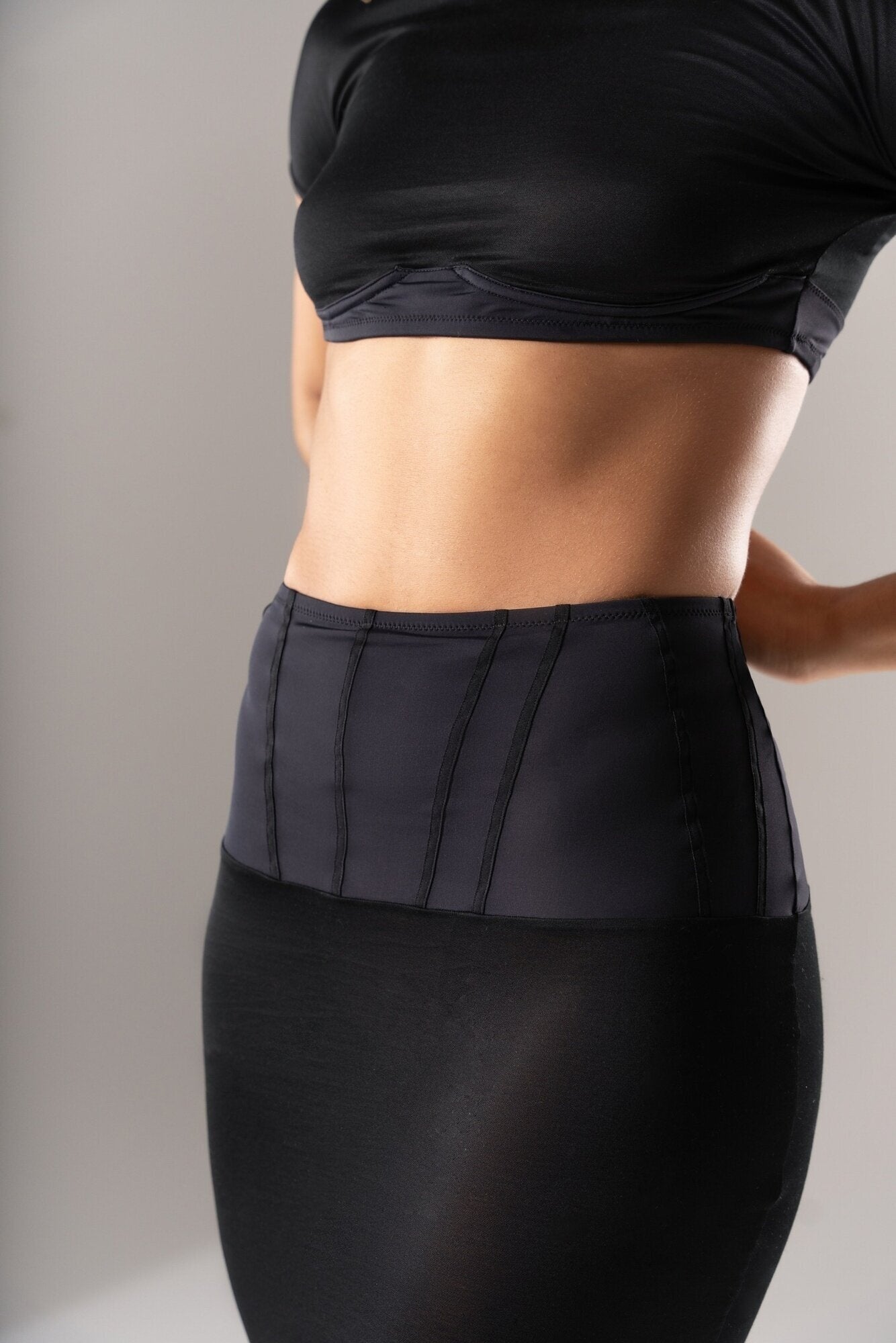 Détail ceinture taille haute de la jupe 03.87, en lycra sculptant avec surpiqûres noires contrastées. Gros plan sur la bande de maintien du top 03.87, en lycra mat structurant sous la poitrine