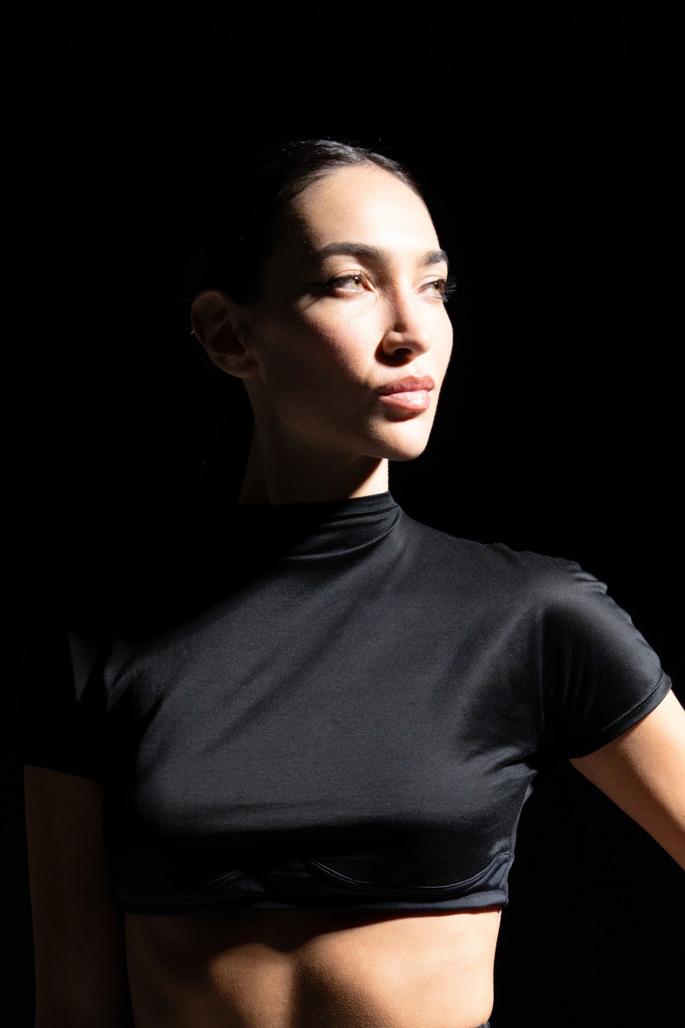 Portrait en gros plan d’un mannequin portant le top court noir 03.87, col légèrement montant et matière satinée