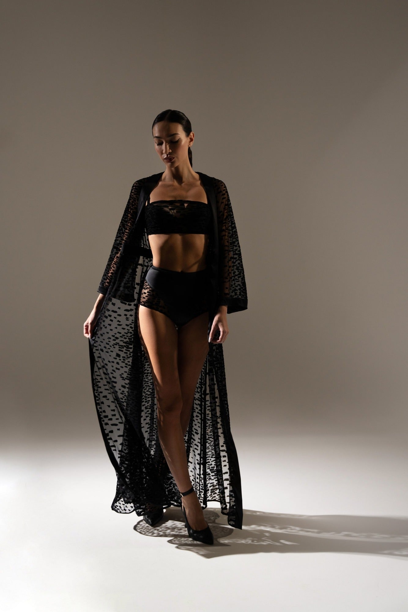 Mannequin défilant en kimono noir long en tulle floqué et lingerie sexy assortie, dans un studio à lumière tamisée