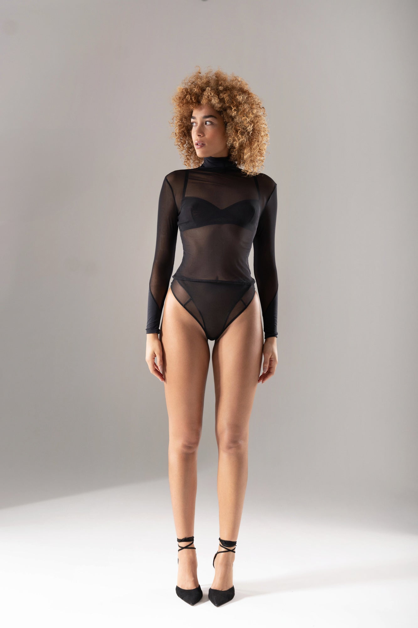 Femme de face portant le Top 10.06 en tulle transparent noir, manches longues et col montant